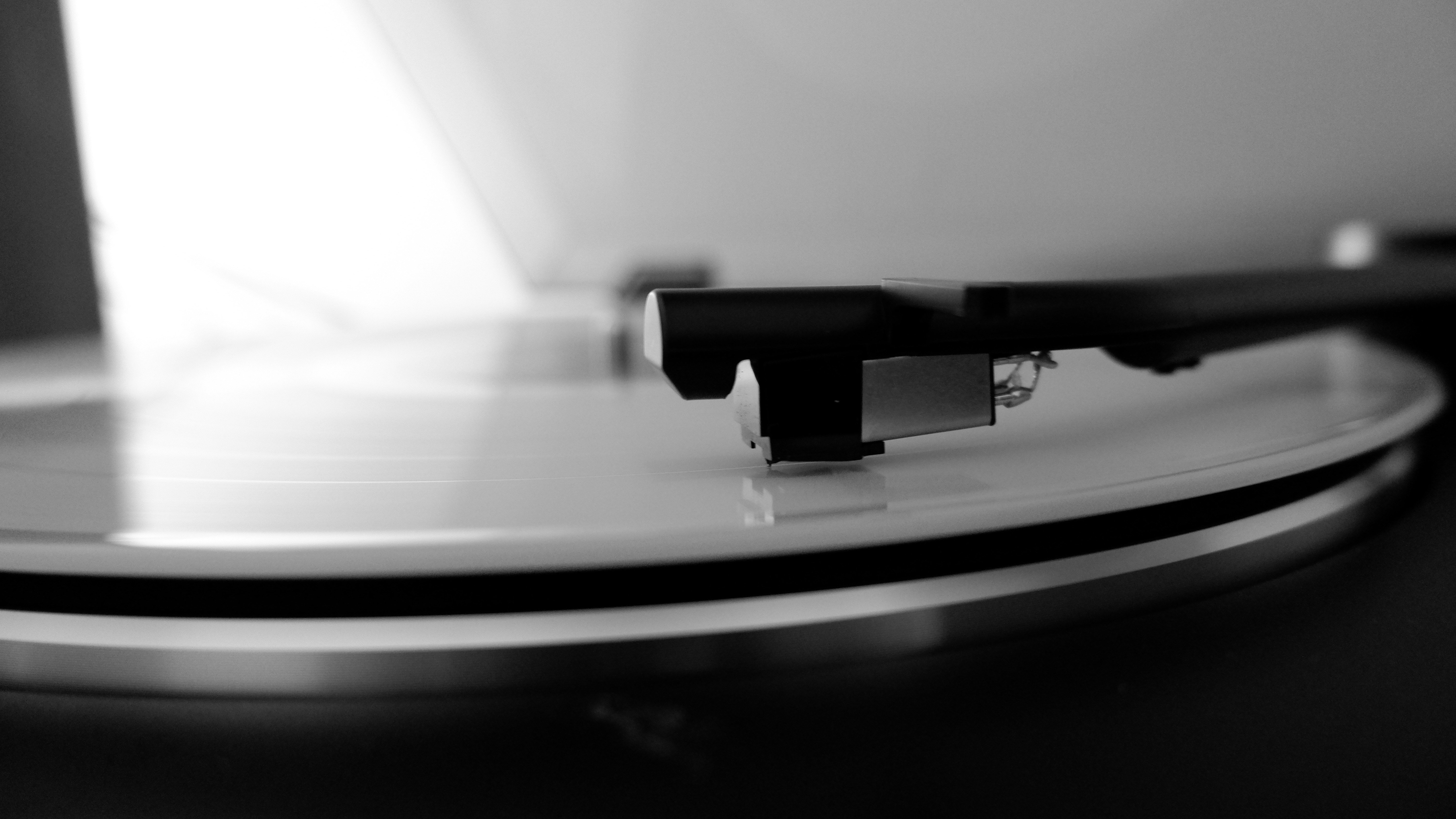 A black and white close up image of a record player needle arm on a vinyl LP.
